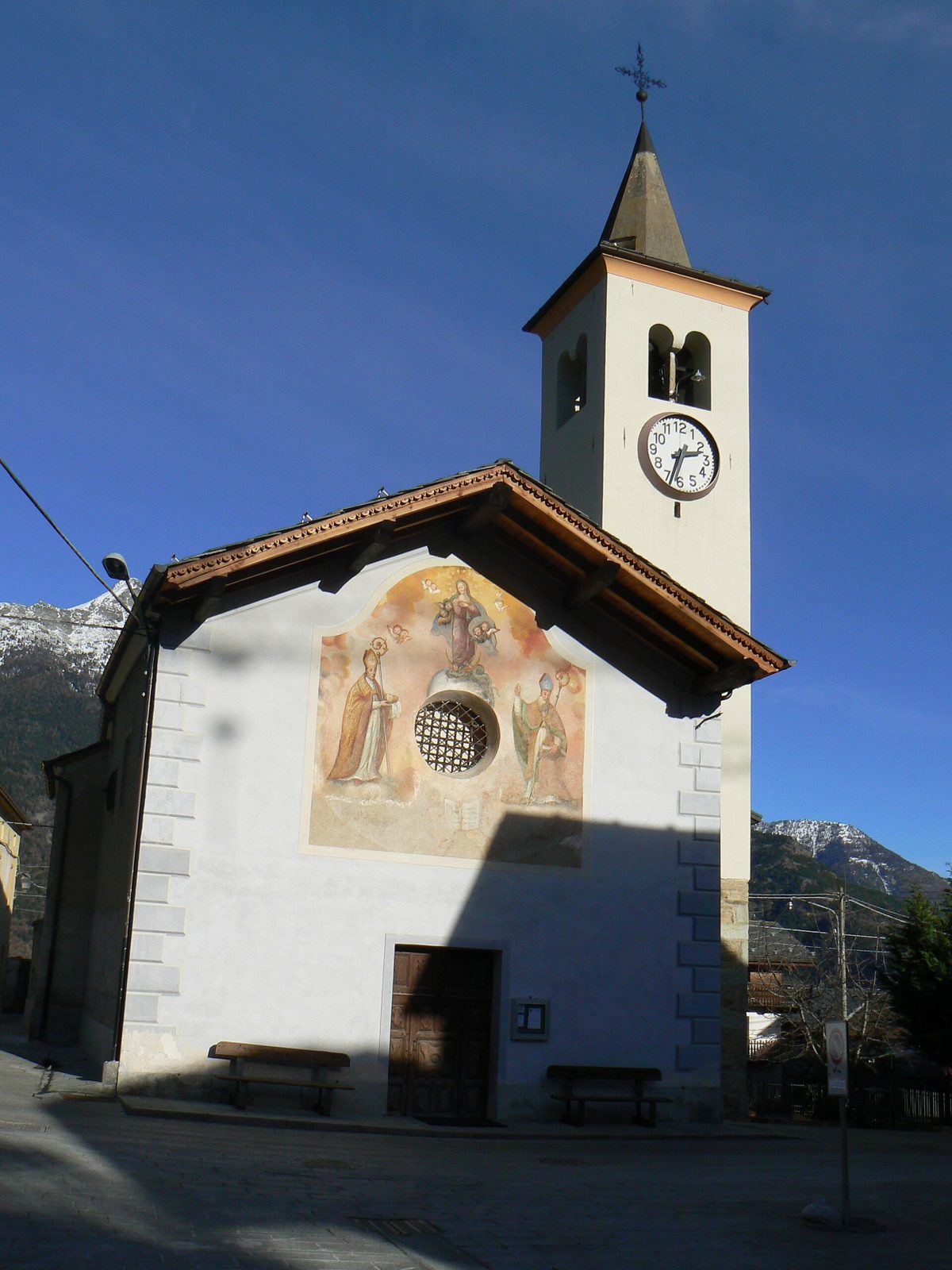 La chiesa di Excenex con il campanile e la facciata affrescata, sullo sfondo le montagne innevate