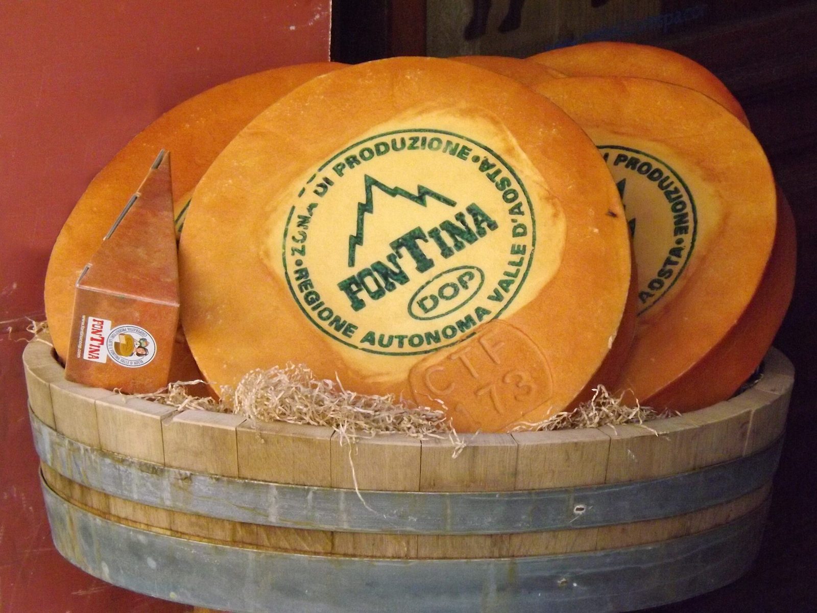 Forme di Fontina DOP con il marchio di produzione della Valle d'Aosta, esposte in una tinozza di legno